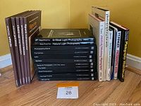 Photo of 15 assorted photography books arranged standing upright on wooden floor against yellow wall, with subject card #28 present.