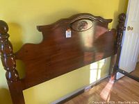Full view of wooden headboard attached to bed frame showing carved central motif and turned posts.