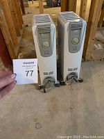 Pair of white DeLonghi oil-filled radiator heaters side by side showing front control panels and base wheels.