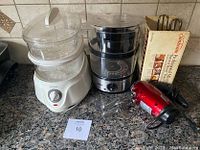 Photo showing Rival and Nesco steamers side by side, along with two Sunbeam hand mixers on a kitchen countertop.