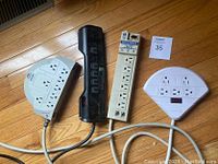 Photo shows four surge protectors of varying styles and colors placed on a wooden floor.