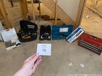 Five tools and tool cases on concrete floor including a red metal Craftsman toolbox, blue Makita Sawzall case, black and yellow Poulan chainsaw, white Workforce tile cutter, and a black tool kit.
