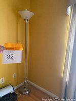 The floor lamp is seen unlit next to a wall in a room with yellow walls and hardwood floor.