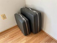 Two black hard suitcases, one large and one carry-on, stacked side by side against wall on hardwood floor.