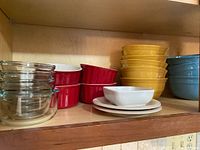 Left side close-up of assorted bowls including clear glass, red ceramic ramikins, white ramikin, and some plates and bowls in yellow and blue.