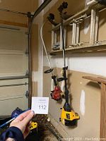 Photo showing two gas weed whackers hanging on wall; red Homelite and yellow Poulan PRO.