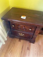 Full view of the wooden nightstand showing carved drawer front details, brass hardware, and polished dark wood finish.