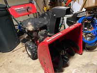 Front angle view of red Yard Machines by MTD snow blower/trimmer unit showing black engine cover, auger housing with blades, and wheels.