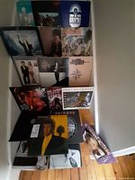 Photo showing 20 vinyl records with visible album covers stacked in multiple layers showing artists and styles from 70s, 80s, and 90s.