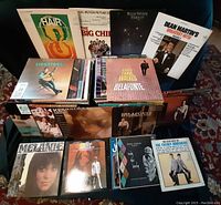 Assorted 51 vinyl LP records arranged with covers facing forward and stacked showing album titles. Visible titles include Hair, The Big Chill, Dean Martin's Greatest Hits, and Harry Belafonte.
