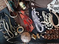 View of assorted vintage necklaces laid out on fabric with multi-strand beaded strands, faux pearls, large pendants.