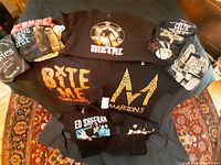 Overhead photo showing all ten concert T-shirts of various bands and artists laid out on a surface with a patterned rug beneath.