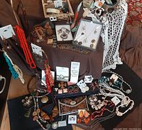 Overview of vintage boho jewelry lot including necklaces, bracelets, earrings, and trinket boxes arranged on dark fabric and a display stand.