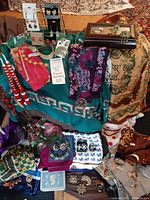 Photo displaying a variety of vintage scarves, earrings, brooches, necklaces, and a jewelry box arranged on fabric backgrounds.