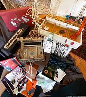Photo showing an assortment of vintage jewellery including necklaces, brooches, earrings, scarves, and jewellery boxes laid out on a dark cloth and nearby chair.