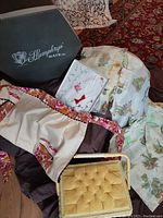 Photo showing vintage linens, Humphreys of London hat box, and yellow sewing notions box together on a dark surface with a floral fabric background.