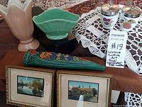 Two framed mini paintings, two Royal Worcester egg coddlers with lids, green ceramic dish, pink vase, floral wall sconce on table with lacecloth and tag.