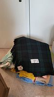 Three folded wool blankets stacked, dark tartan blanket on top with Kayso label visible on next photo