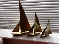 All three brass sailboat sculptures displayed on a windowsill