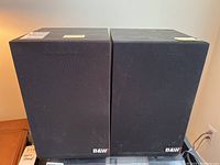 Two black B&W speakers side by side with fabric covers and B&W logos visible on front bottom right corners.