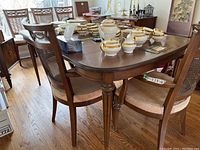 Dining table shown with multiple chairs and porcelain serving set on top to illustrate size and style.