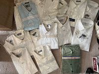 Overview of multiple men's dress shirts in various colors including white, cream, blue, and green, some in plastic packaging.