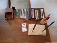 Overview of all items: Parker pens in cases laid out, onyx flat pen stand with two pens, onyx cylindrical pen holder with pens, golf style metal pen stand, and wooden box with hinged lid