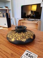 Front and side view of the squat black vase with detailed gold decorative pattern on a wooden table.