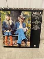 Front cover of ABBA Greatest Hits vinyl album showing two band members seated outdoors on a bench.