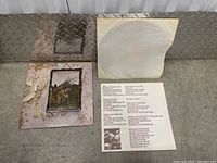 Vinyl record partially removed from plain paper sleeve and lyric insert with printed lyrics and black and white photo of band members.