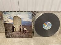 Front of album cover with band members and monolith under cloudy sky