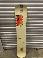 Topside of snowboard showing cream background with orange and red geometric dot graphics and Ride brand logo near tail.