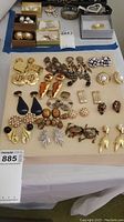 Photo showing an assortment of 19 pairs of costume earrings in various shapes, sizes, and decorative styles laid flat on a beige surface.