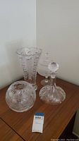 Four crystal items grouped on table showing decanter, vase, bowl, and frosted compote