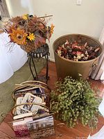 Photo showing magazine racks with books and magazines, faux green plant in front, large gold-toned planter with floral arrangement in background.
