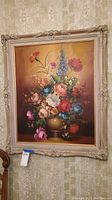 Full view of the ornately framed floral painting hanging on the wall, showing the entire piece and frame details.
