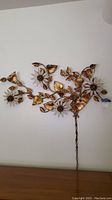 Front view of gold-tone metal floral wall sculpture hung on white wall