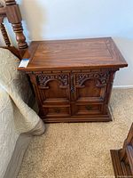 Front view of wooden nightstand showing cabinet door with carvings and two drawers