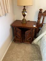 Wooden nightstand next to bed, showing cabinet doors closed and design details