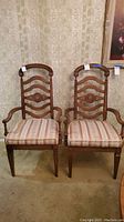 Pair of two wooden arm chairs with padded upholstery, placed side by side against wallpapered wall.