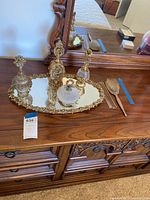 Four ornate vintage perfume bottles displayed on an ornate gold-tone mirrored tray on wooden dresser