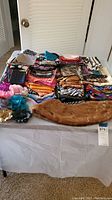 Photo showing a variety of folded silk scarves in multiple bright patterns and colors, placed on a table. Also visible is a light brown faux fur stole and fabric flower accessories.