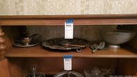Various serving pieces: pewter plate, repousse crumber brush and pan, frosted glass oyster shell shaped bowl on shelves