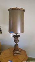Full view of table lamp showing tall cylindrical bronze shade and decorative base.