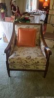 Front view of vintage wood framed armchair with floral upholstery and orange cushion on seat