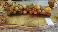 Full view of the curved wooden vine base holding a cluster of glass grapes in amber and brown hues with green leaves.