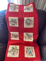 Full view of unfolded quilt on couch showing red and cream panels with embroidered states including Texas, Missouri, and others.