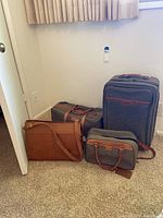 Four pieces of luggage including the large suitcase, duffel bag, small carry bag, and briefcase all arranged on carpet beside a wall.