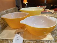 Three yellow vintage mixing bowls with white interiors on countertop, different sizes.