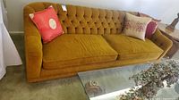Front view of entire mustard yellow tufted sofa with two seat cushions and pillows.